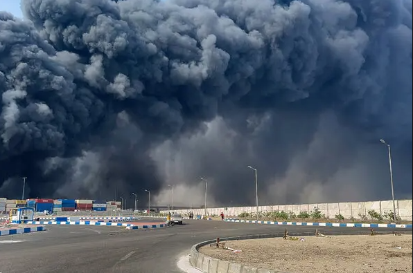 An image showing a massive fireball rises into the night sky following the devastating explosion at Iran’s Bandar Abbas Port, with thick smoke and debris filling the air.