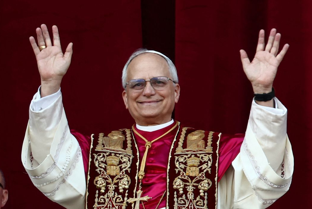 An image of Pope Leo XIV, formerly Cardinal Robert Francis Prevost, stands on the balcony of St. Peter's Basilica, giving his first blessing to the crowds below. He is wearing papal vestments.