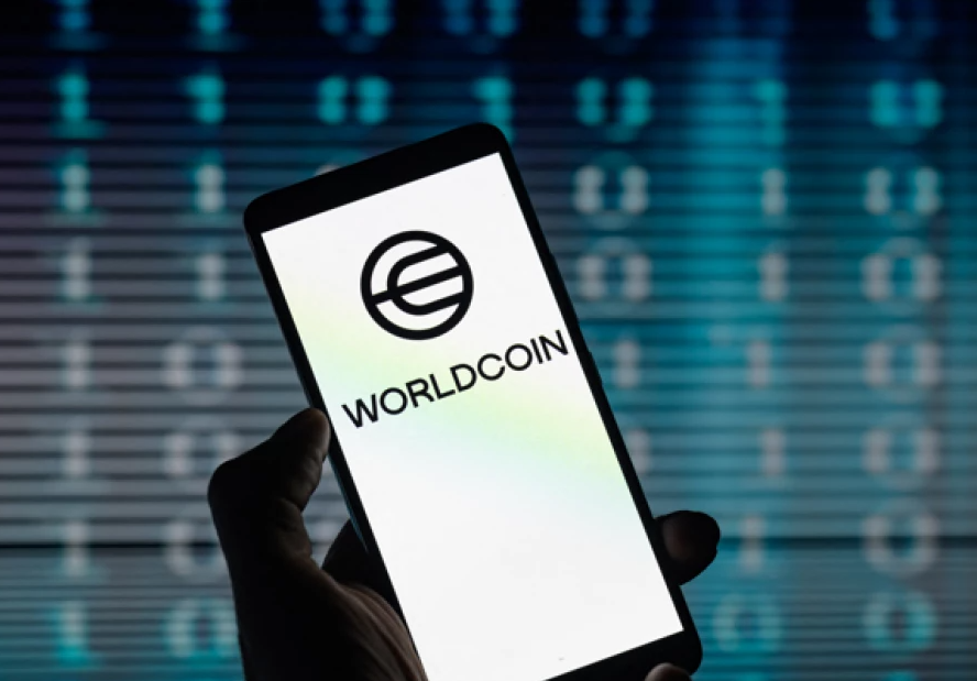The Worldcoin logo, a stylized silver orb with intersecting lines, displayed prominently on a bright digital screen.